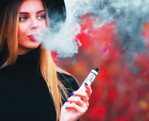 Junge hübsche Frau im Hintergrund bläst Vape Rauch auf einem roten Hintergrund