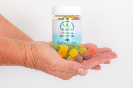 Rainbow CBD gummies and jar displayed in hands - The Real CBD Brand