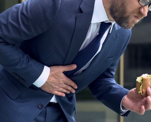 Mann mit Essen in der Hand, der sich vor Schmerzen bückt