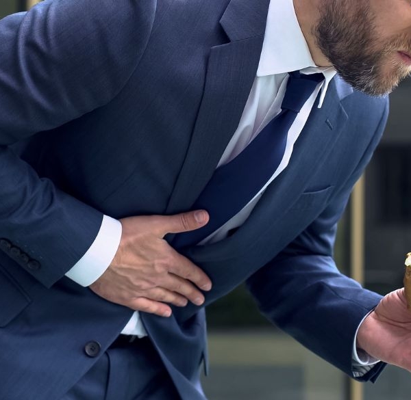 Mann mit Essen in der Hand, der sich vor Schmerzen bückt