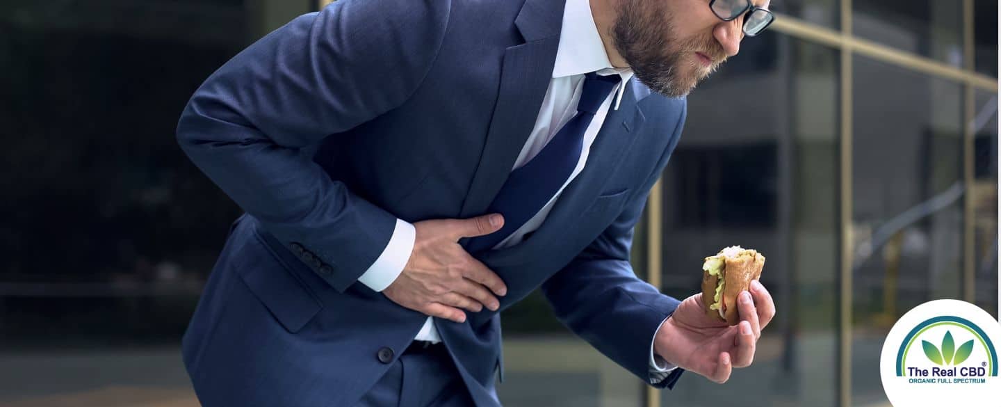 Mann mit Essen in der Hand, der sich vor Schmerzen bückt