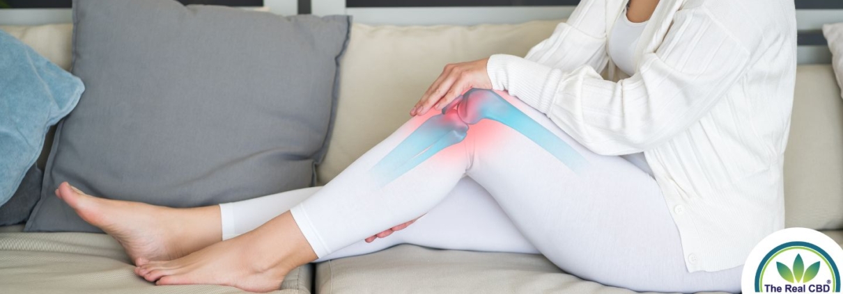 Woman sitting on a sofa, holding her knee joint in pain