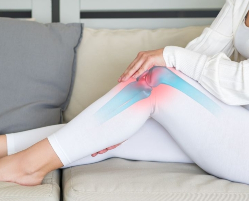 Woman sitting on a sofa, holding her knee joint in pain