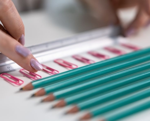 Pencils and paper clips laying in neat lines with a ruler fingers organising it