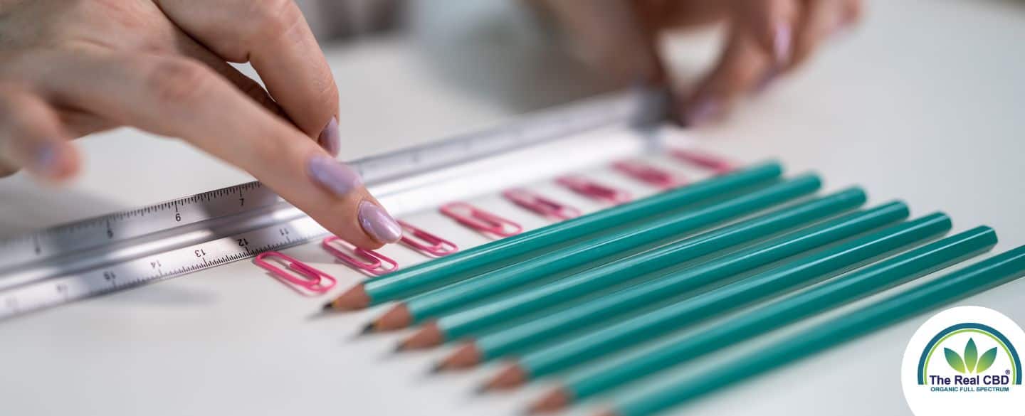 Pencils and paper clips laying in neat lines with a ruler fingers organising it