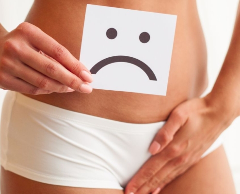 Woman holding an unhappy sign in front of her pelvis