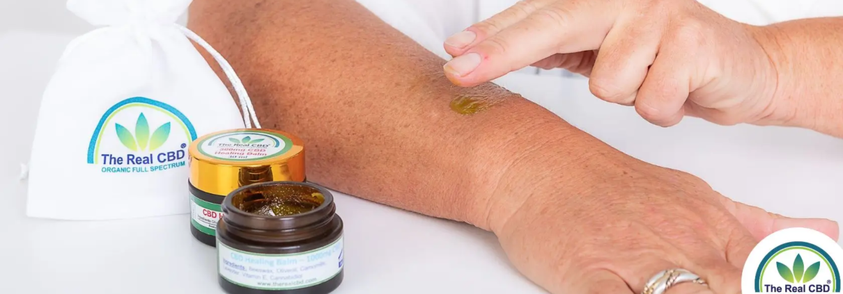 Hand, die The Real CBD Balsam auf den Arm reibt