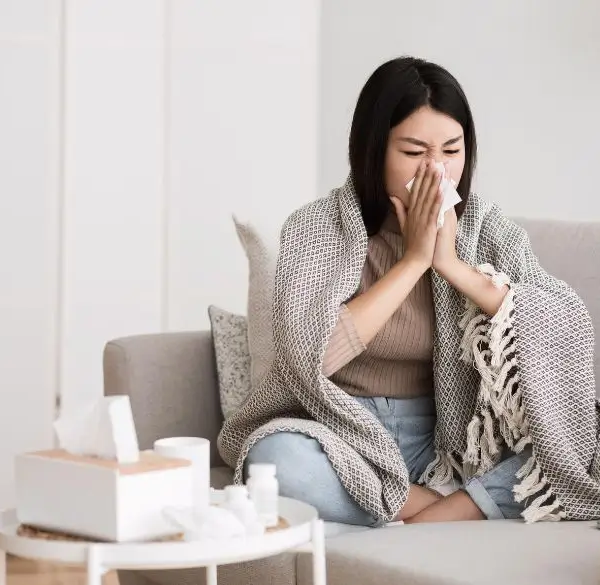 Woman with a clod on the sofa while blowing her nose