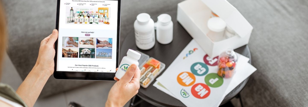 Ein Mann hält ein Tablet mit der The Real CBD Website und ein Glas mit The Real CBD Tabletten